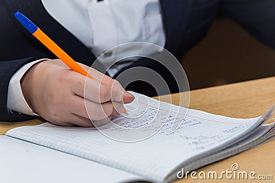 The boys hand with a fountain pen with blue ink solves math examples. Stock Photo