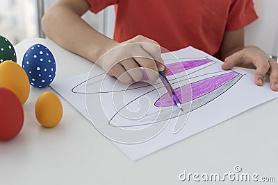 Boys hand hold pencil and paint bunnys ears for easter holiday, colored eggs are near on white table. Stock Photo