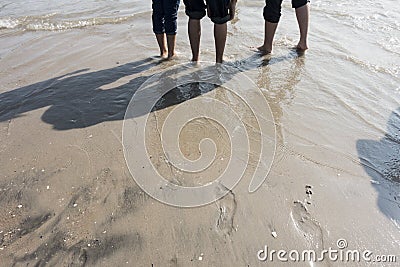 Boys with rolled up paint on the wet sandy beach footprint on wet sand and feet Stock Photo