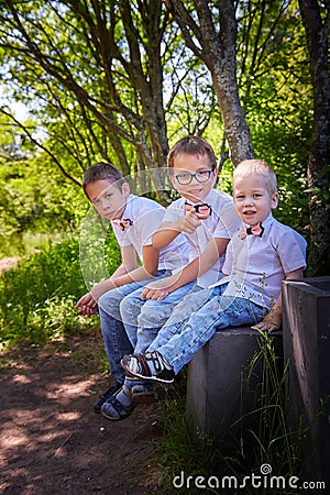 Boys in a white shirts and a pink butterfly in nature among the greenery. Funny walk of three brothers in the park or forest Stock Photo