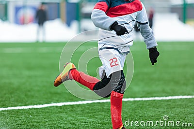 Boys in white sportswear running on a soccer field with snow in the background. Stock Photo