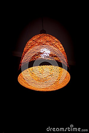 A braided orange retro lampshade with one wooden-style light bulb on a dark background. Detail of the interior. Light. Conceptual Stock Photo