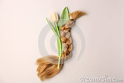 Braided strand and flower on light background. Concept of hair donation Stock Photo