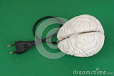 Brain with an electric wire for charging on a green background. Stock Photo