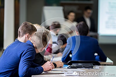 Brainstorming, young students 18-20 years old, vividly discuss the lecture of teachers at the table, take an exam, write and Editorial Stock Photo