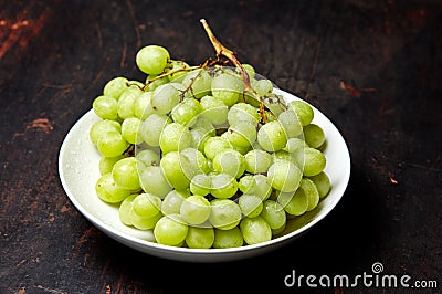 Branch of ripe green grape on plate with water drops. Juicy grapes on wooden background, closeup Stock Photo