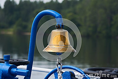 Brass bell on the foredeck of a ship against the background of a blurred wooded coast Stock Photo