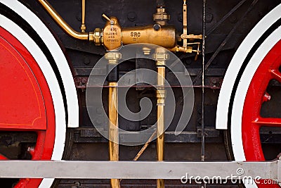 Brass-colored steam locomotive train part bordered by two red wheels Stock Photo