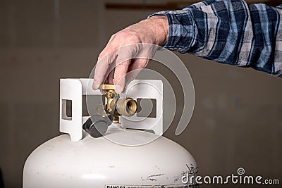 Man opens the valve knob on the top of a propane bottle Stock Photo