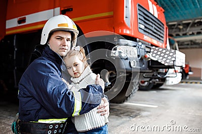 Brave firefighter in uniform holding little saved girl standing on black background Stock Photo