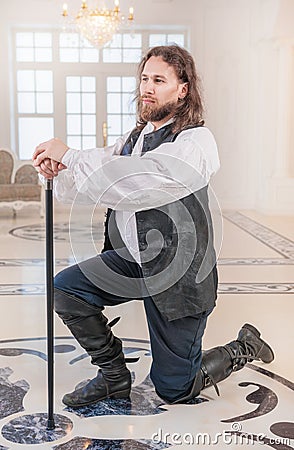 Brave man in medieval clothes with cane standing on knee Stock Photo