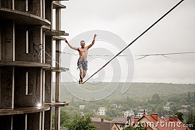 Brave man balancing on a slackline high against empty building and sky Stock Photo