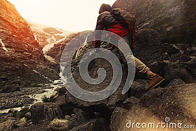 Brave traveler with a backpack climbing on a rock, against the backdrop of a glacier Stock Photo