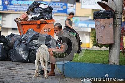 Brazil- street dweller seated next to trash can and trash bags Editorial Stock Photo