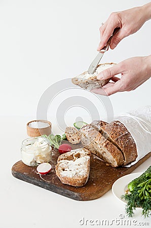 Bread with salt, butter, cucumber and radishes lie on a white background. A girl is buttering a sandwich. Stock Photo