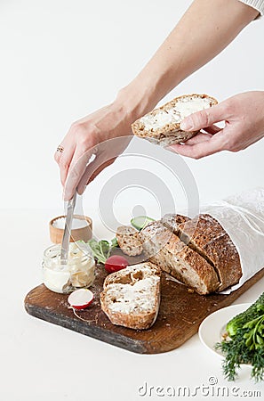 Bread with salt, butter, cucumber and radishes lie on a white background. A girl is buttering a sandwich. Stock Photo