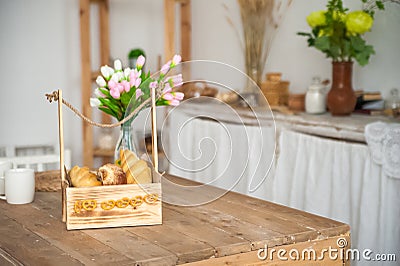 Bread in a textured wooden box in the kitchen in a rustic style. Breakfast, bread, white cups in the interior of bright Scandinavi Stock Photo