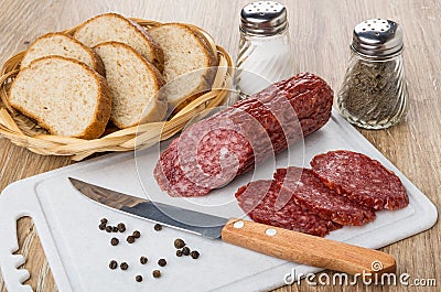 Bread in wicker basket, slices of smoked sausage and knife Stock Photo