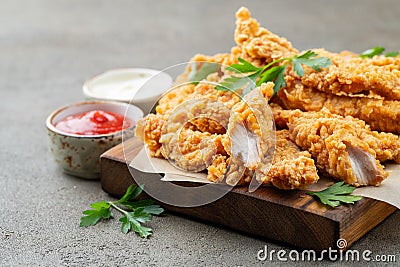 Breaded chicken strips with two kinds of sauces on a wooden Board. Fast food on dark brown background Stock Photo