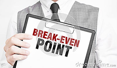 BREAK-EVEN POINT inscription on a notebook in the hands of a businessman on a gray background, a man points with a finger to the Stock Photo