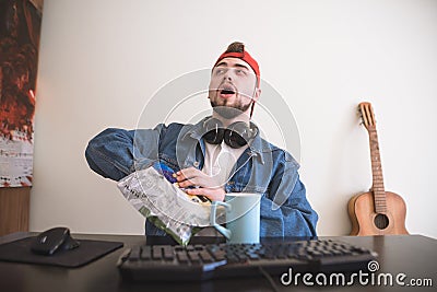 . Break in the game. A funny gamer eats snacks from a pack while gaming at home and a computer Stock Photo