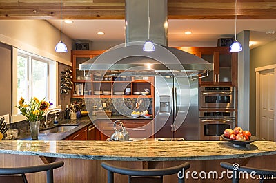 Breakfast bar in contemporary upscale home kitchen interior with granite countertops, vent hood and accent lighting Stock Photo