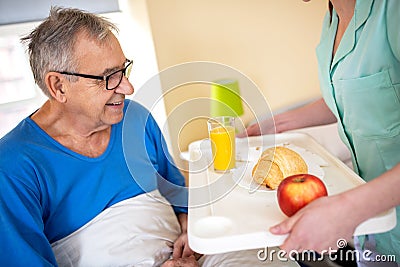 Breakfast in bed, residential care in a nursing home, elder man nursing home occupant being served breakfast by a nurse Stock Photo