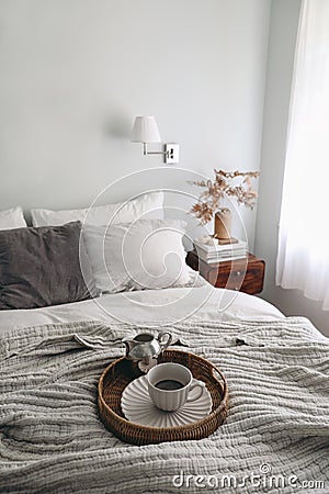 Breakfast in bed scene. Cup of coffee, silver milk pitcher on wicker tray and linen blanket. Blurred pillows, night Stock Photo