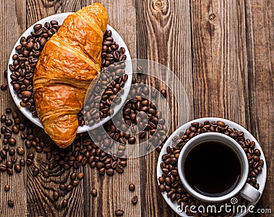 Breakfast coffee - cup and croissant with coffee beans on wooden background. Stock Photo