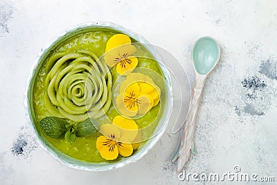 Breakfast detox green smoothie bowl topped with kiwi rose and edible Pansy flowers. Stock Photo