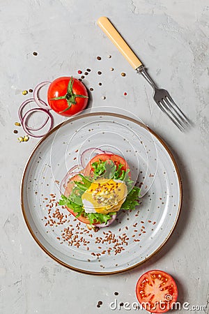 Poached egg sandwich with hollandaise sauce, tomatoes and onions on a gray plate. eggs Benedict. Overhead,vertical, with Stock Photo