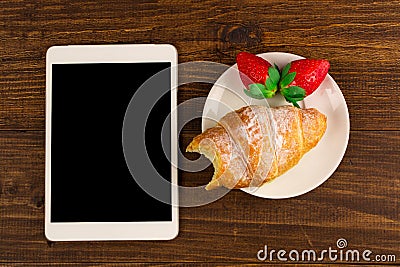 Breakfast with fresh croissants, fresh strawberry on a rustic wooden background, top view. tablet pc. Stock Photo