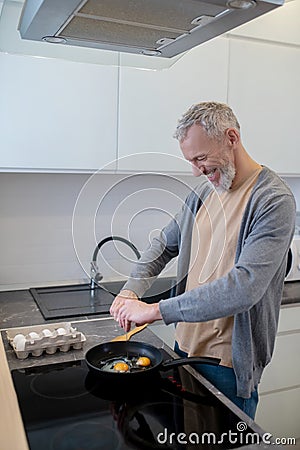 A gray-haired man cooking omlette in the kitchen Stock Photo