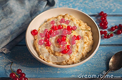 Breakfast of milk oatmeal with red currants on a blue wooden tray, spoon and denim napkin, as well as sprigs of currant, taken Stock Photo