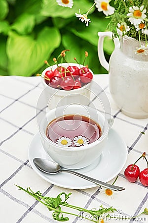 Breakfast outside. Cup of tea, strawberries, cherries, chamomile bunch on table. Summer picnic. Good morning concept Stock Photo