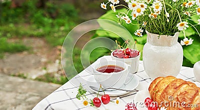 Breakfast outside. Cup of tea, strawberries, cherries, croissants, chamomile bunch on table. Summer picnic. Good morning concept Stock Photo