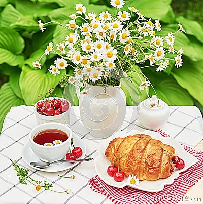 Breakfast outside. Cup of tea, strawberries, cherries, croissants, chamomile bunch on table. Summer picnic. Good morning concept Stock Photo