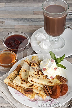 Breakfast. Pancakes, honey, strawberry jam, cream, dried apricots, nuts and hot chocolate or cocoa or coffee Stock Photo
