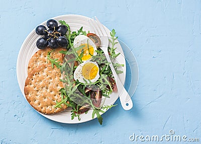 Breakfast plate - whole wheat cracker, arugula, cherry tomatoes, boiled egg salad on blue background Stock Photo