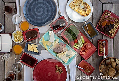 breakfast prepared on wooden table, cheeses, jams, tomatoes, cucumber, smoked meat, butter, honey, olives, breads Stock Photo