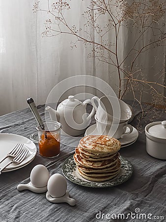 Breakfast served on the table - pancakes, apricot jam, boiled eggs in ceramic egg stands, breakfast dishes on the table with a Stock Photo