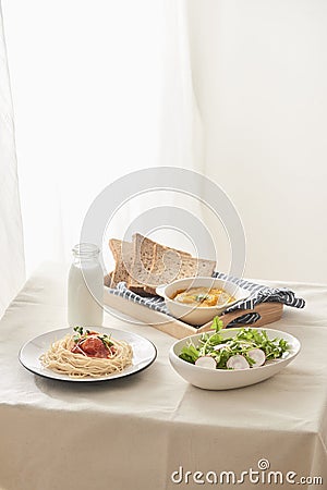 Breakfast table; spaghetti served with radish and salad with pumpkin puree, bread, milk set on table Stock Photo