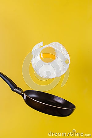 Breakfast time. A fried egg and a frying pan levitate in the air on a yellow background. Stock Photo