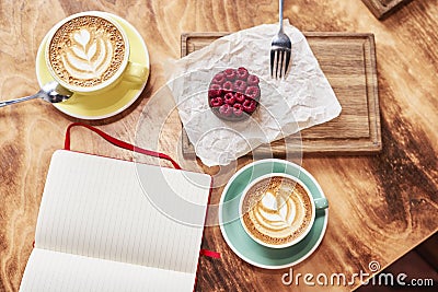 Breakfast time with two cups of fresh coffee from above on wooden background, sweet strawberry cake on wood board, opened book Stock Photo