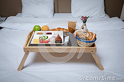 Breakfast on a white plate on a wooden tray with legs lying on a white blanket and bed.Isolated on bed background and two white pi Stock Photo