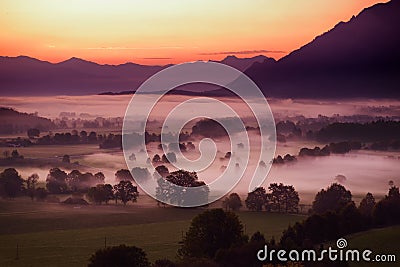 Breathtaking morning lansdcape of small bavarian village covered in fog. Scenic view of Bavarian Alps at sunrise with majestic mou Stock Photo