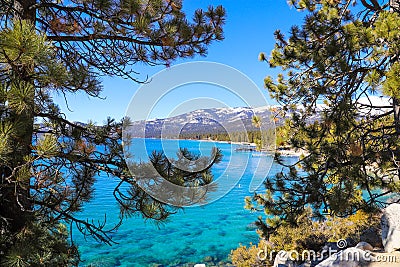 A breathtaking shot of vast blue lake water and lush green trees and snow capped mountain ranges Stock Photo