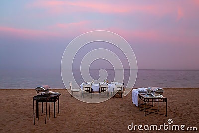 A table and chairs for a barbecue party on the beach, at sunset, and a calm sea in the background Stock Photo