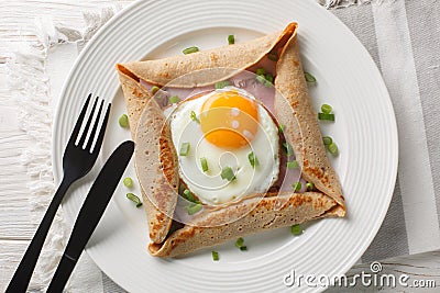 Breton galette, galette sarrasin, buckwheat crepe, with fried egg, cheese, ham closeup on the plate. Horizontal top view Stock Photo