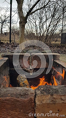 Brick fireplace with bright bonfire inside. Red flames in old burnt mangal. Grunge textures of countryside in cold weather. Stock Photo
